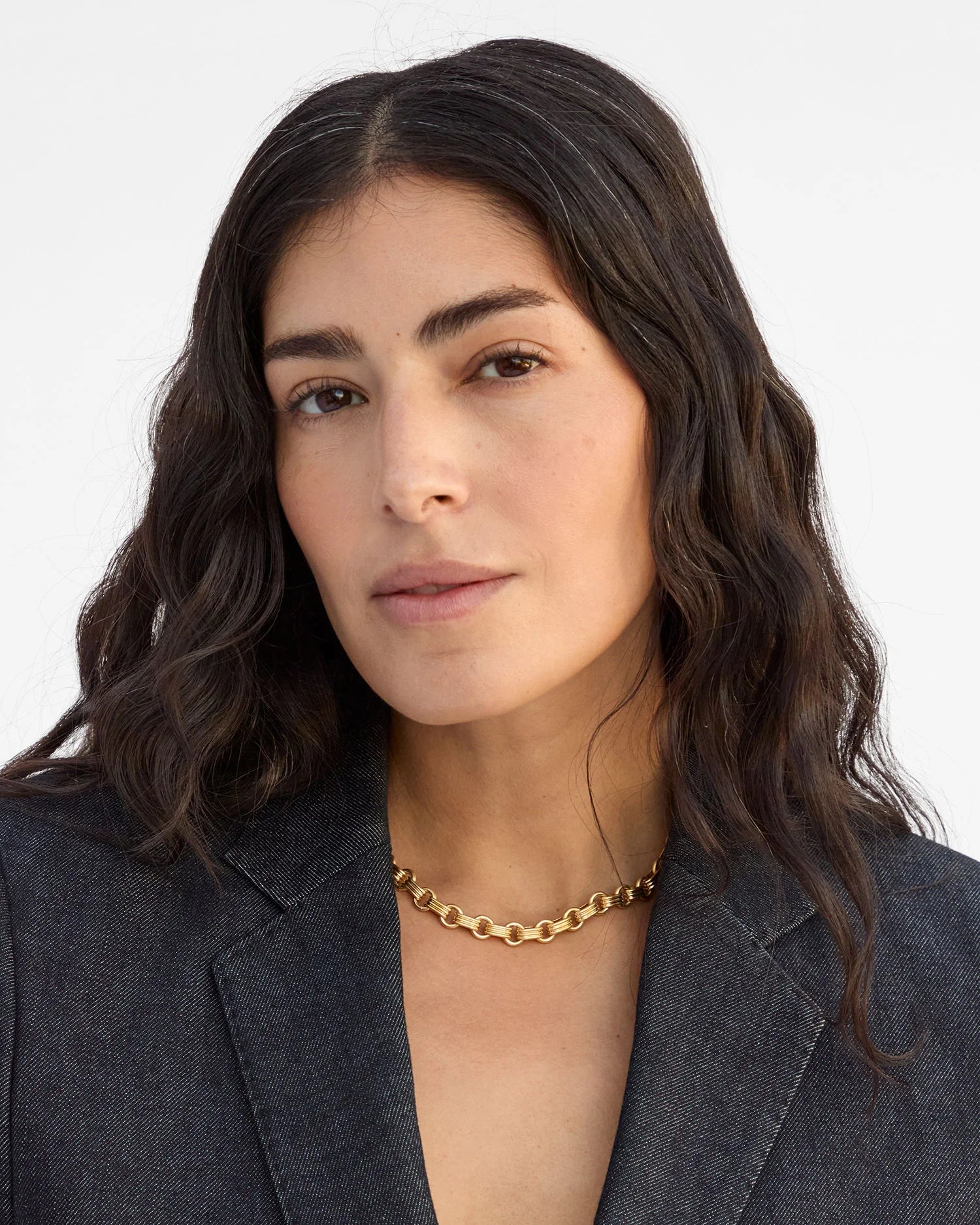 Woman wearing a gold necklace against a plain background