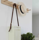 White tote bag with 'FIELDBAR' branding, straw hat, and brown strap hanging on a wooden hook against a white wall.