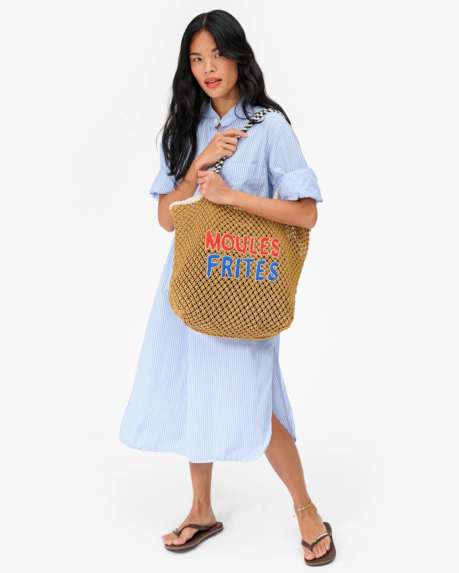 Woman holding a woven bag with text, wearing a light blue dress on a white background