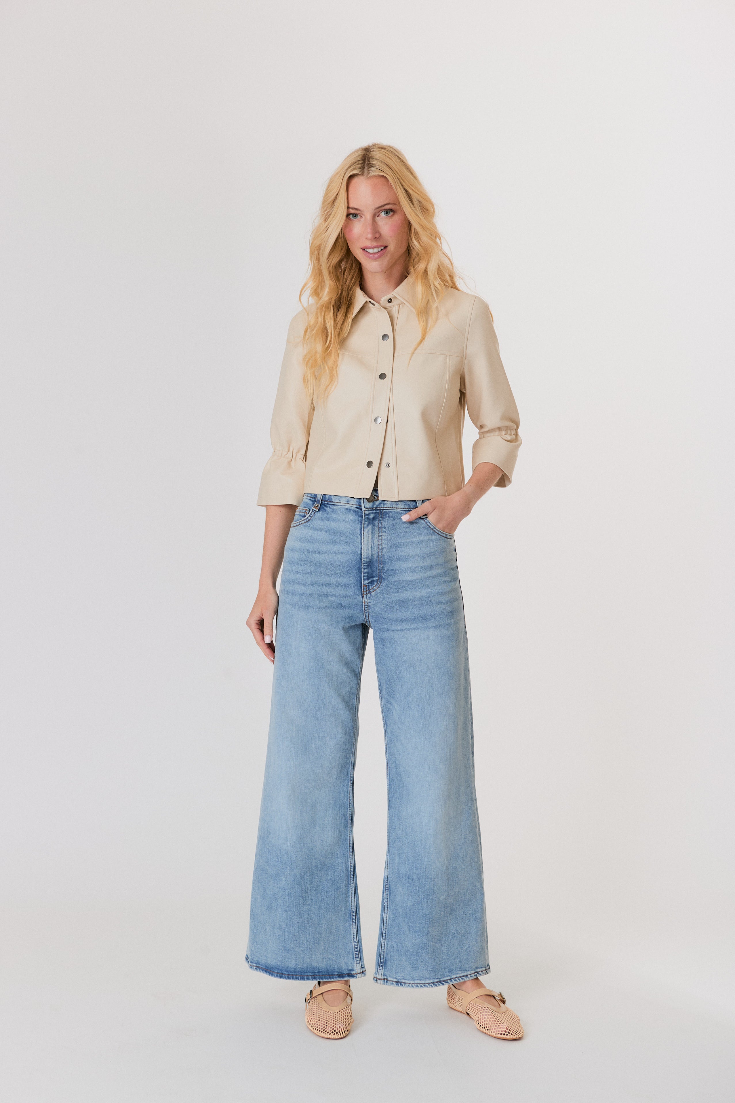 Woman wearing a beige jacket and light blue jeans on a white background