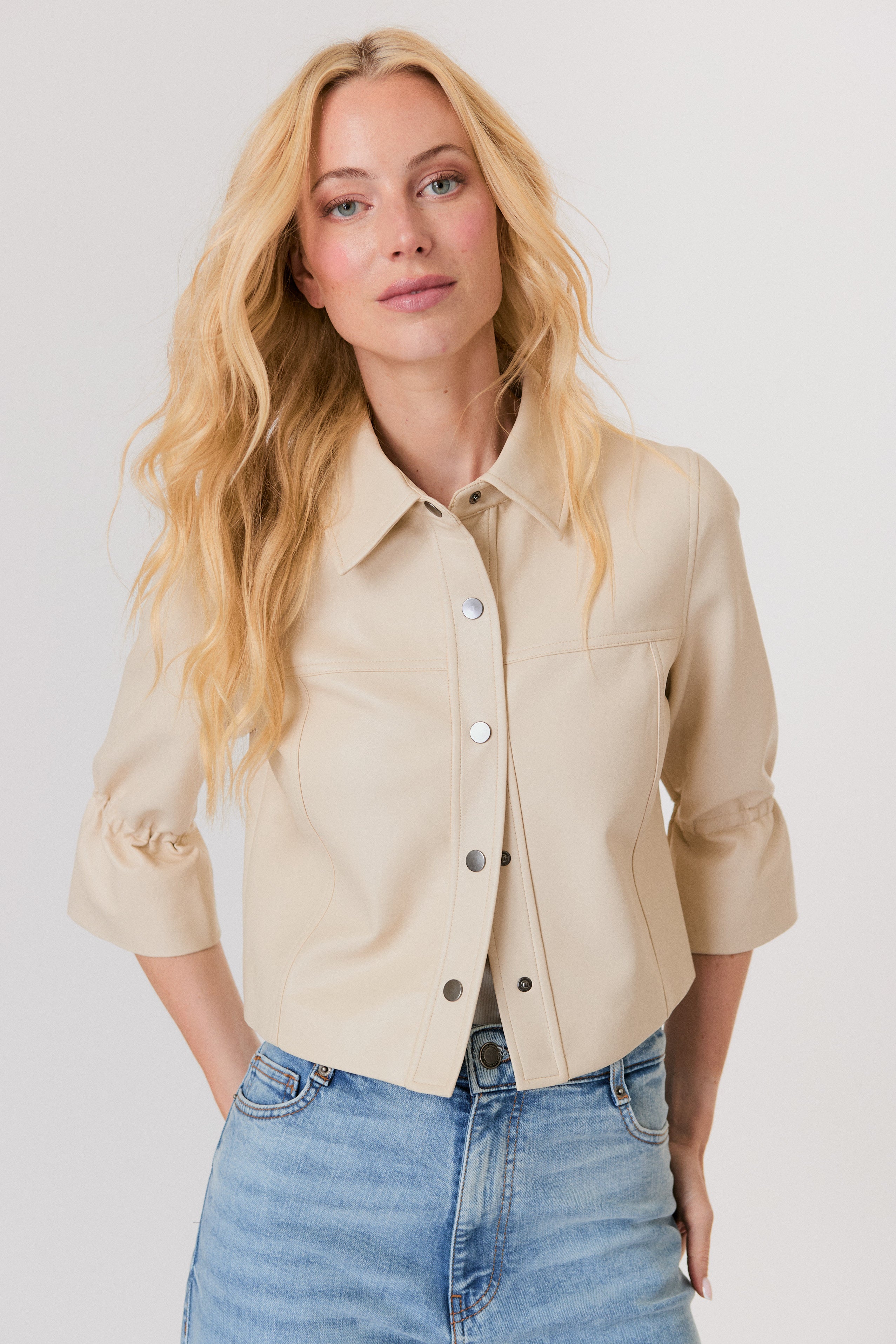 Woman wearing a beige shirt and blue jeans against a white background