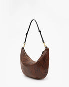 A brown snakeskin-patterned crescent shoulder bag with a black strap and gold-tone hardware, photographed on a clean white background.