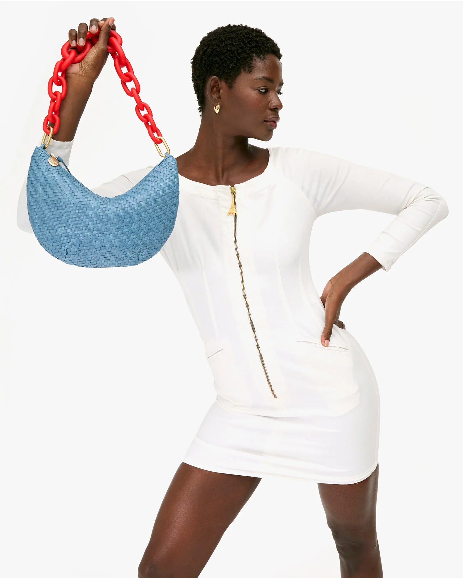 Woman in a white dress holding a blue handbag with a red chain strap on a white background