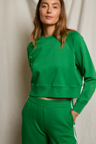 Woman wearing a green sweatshirt and pants against a neutral background