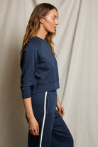 Woman wearing a navy blue tracksuit with white stripes on a neutral background