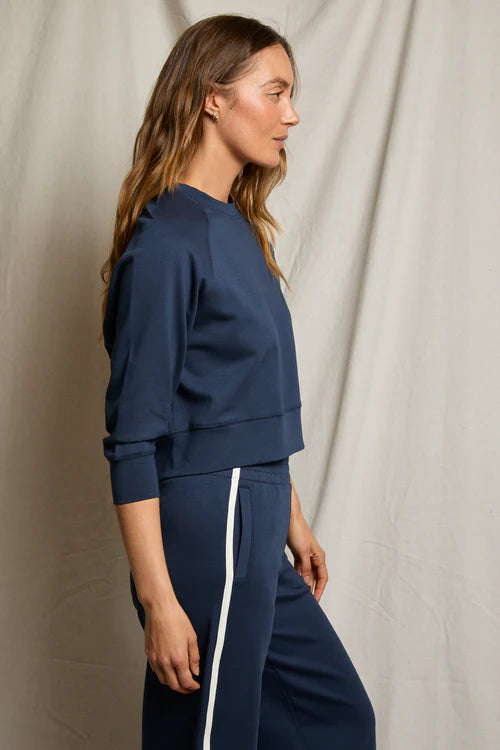 Woman wearing a navy blue tracksuit with white stripes on a neutral background
