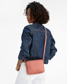 Person wearing a denim jacket with a pink crossbody bag on a white background