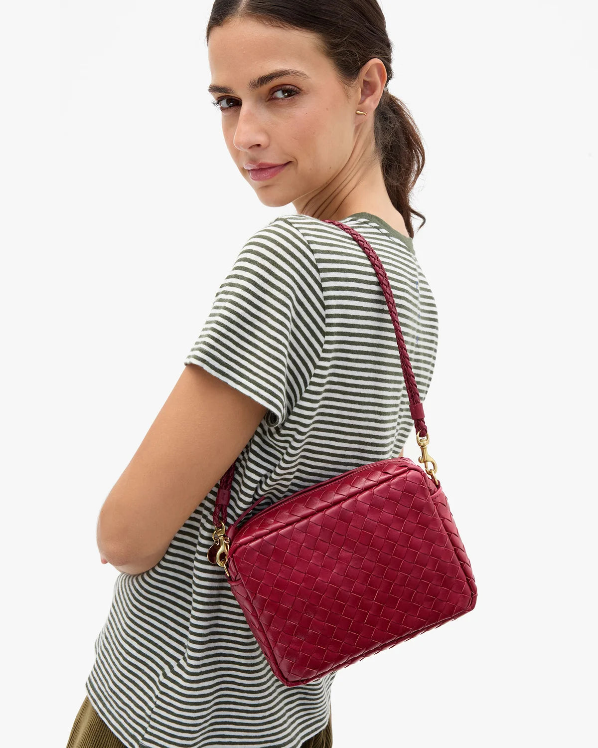 A woman wearing a striped t-shirt models a red woven leather crossbody bag with gold hardware against a plain white background.
