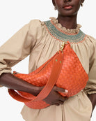 Person holding an orange woven handbag against a neutral background