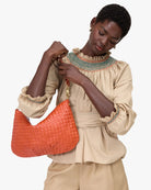 Woman holding an orange woven handbag against a white background