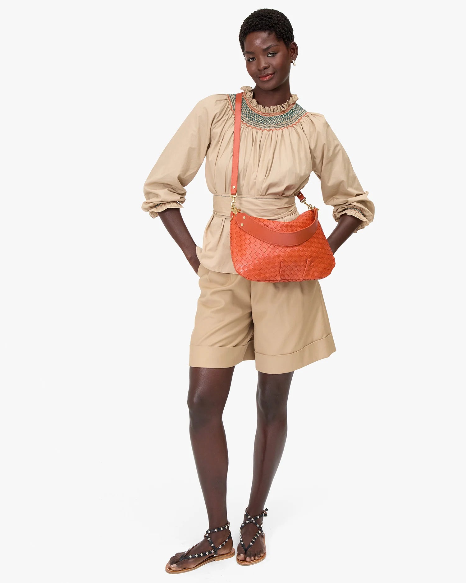Woman wearing a beige outfit with a red bag on a white background