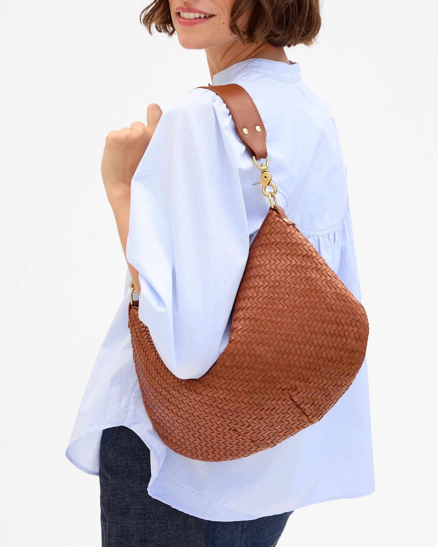 Person wearing a brown woven handbag over one shoulder on a white background