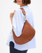Person wearing a brown woven handbag over one shoulder on a white background