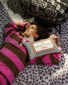 Woman in a pink and brown robe lying on a patterned rug with a pillow that says 'Espresso Martinis, please.'