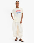 Woman wearing a white t-shirt with 'MOULES FRIITES' text and white pants on a white background