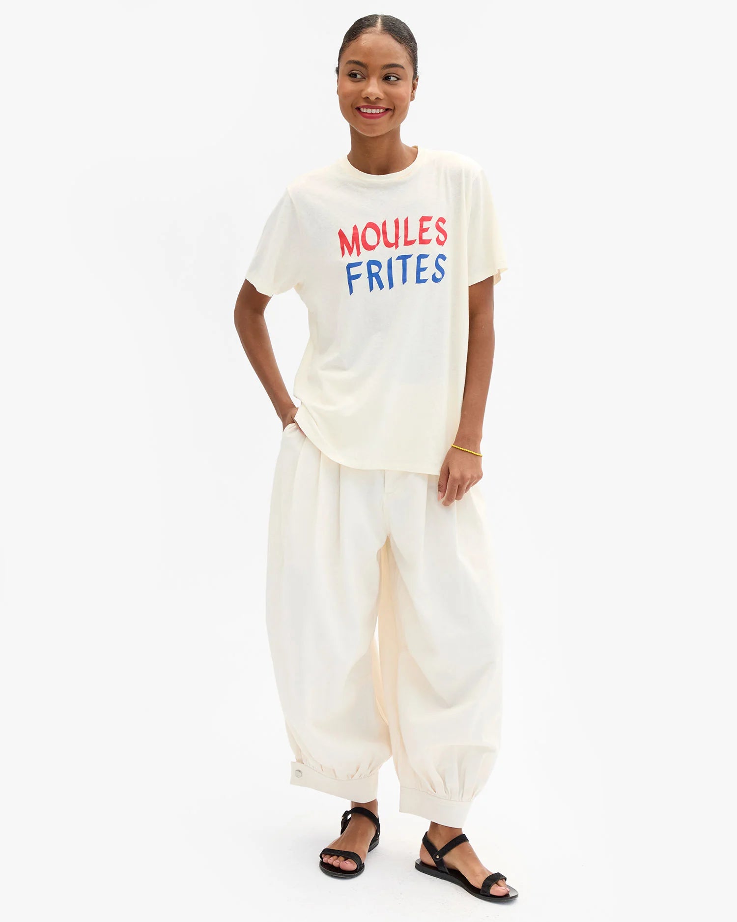 Woman wearing a white t-shirt with 'MOULES FRIITES' text and white pants on a white background