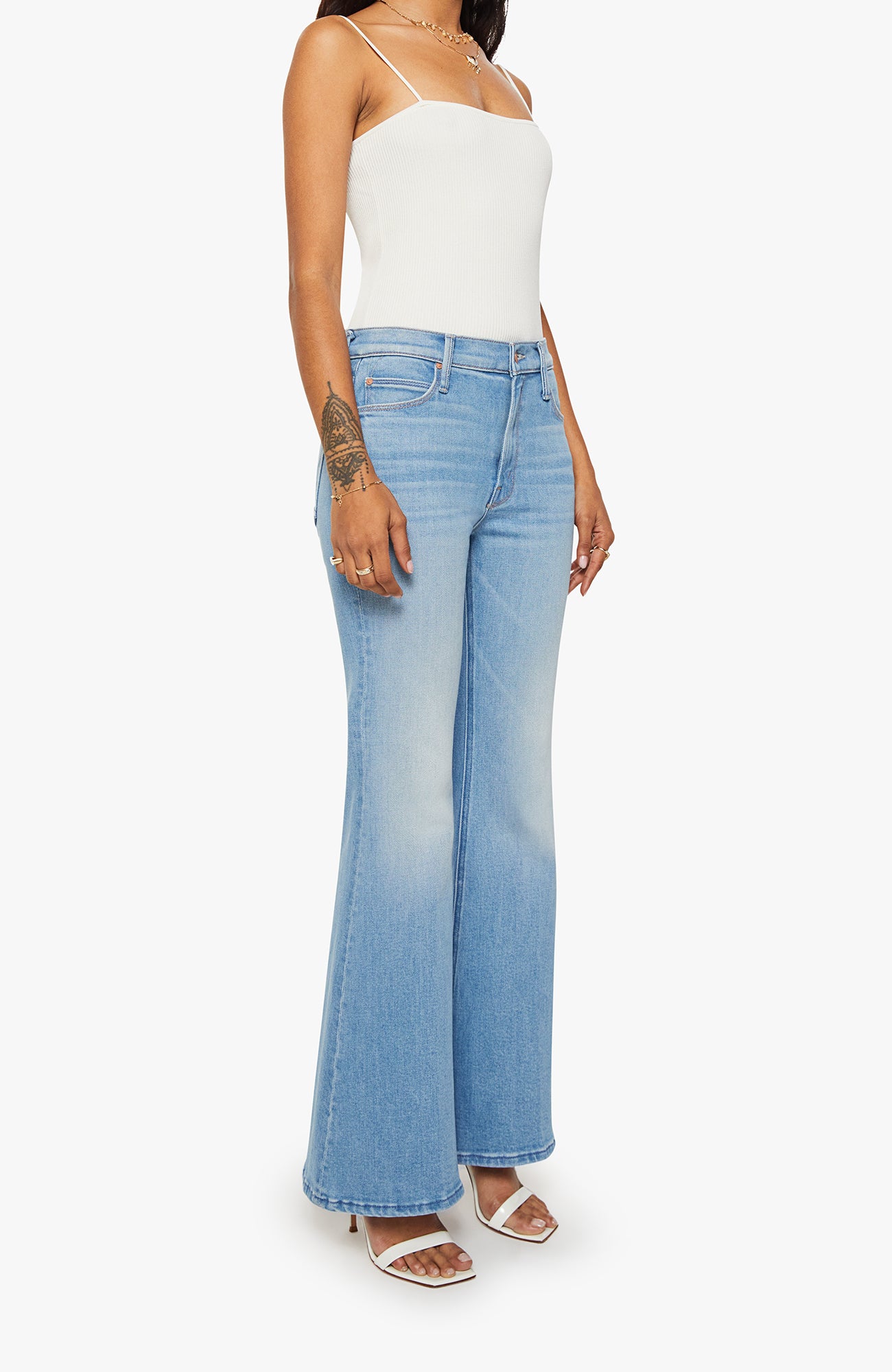 Woman wearing light blue flared jeans and a white top on a white background