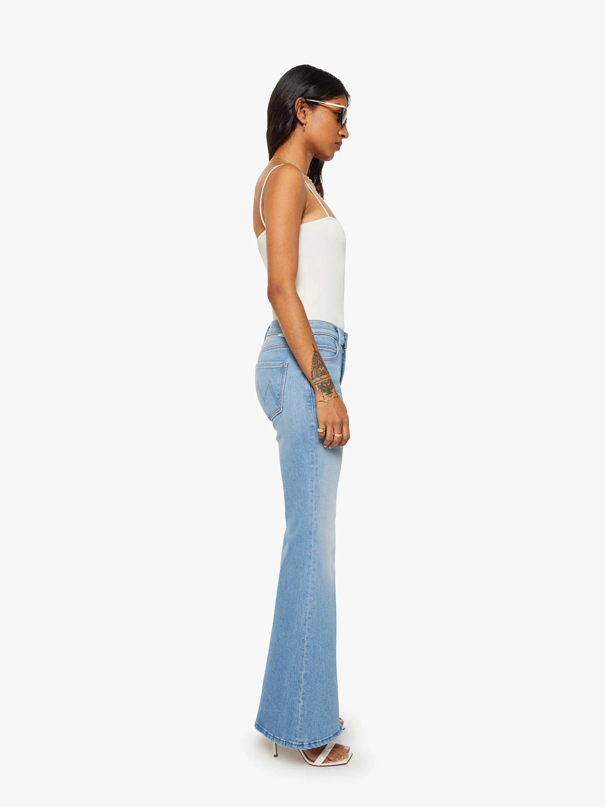 Woman wearing light blue flared jeans and a white top on a white background