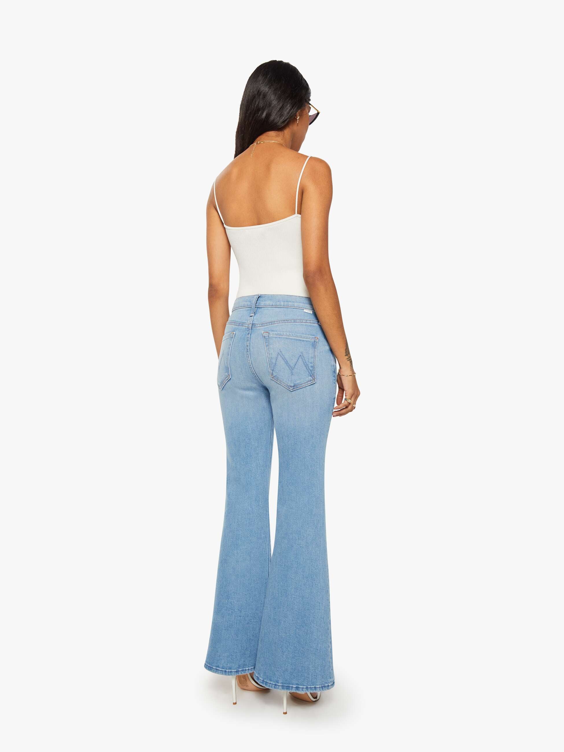 Woman wearing light blue flared jeans and a white top on a white background