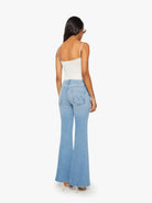Woman wearing light blue flared jeans and a white top on a white background