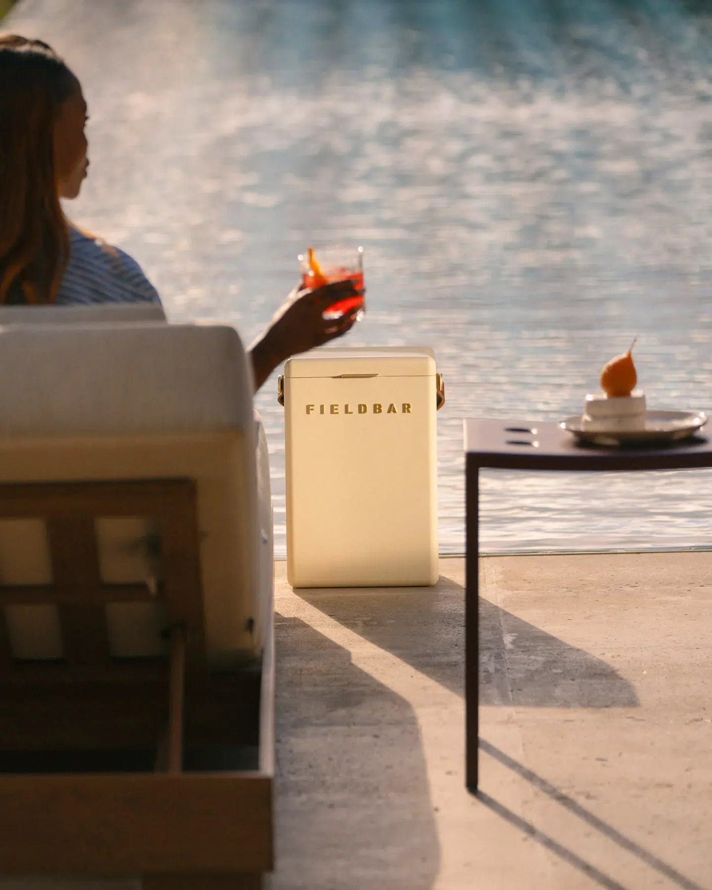 Person sitting by a poolside holding a drink, with a Fieldbar cooler in the foreground.