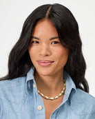 Woman wearing a blue denim shirt and a necklace on a plain background