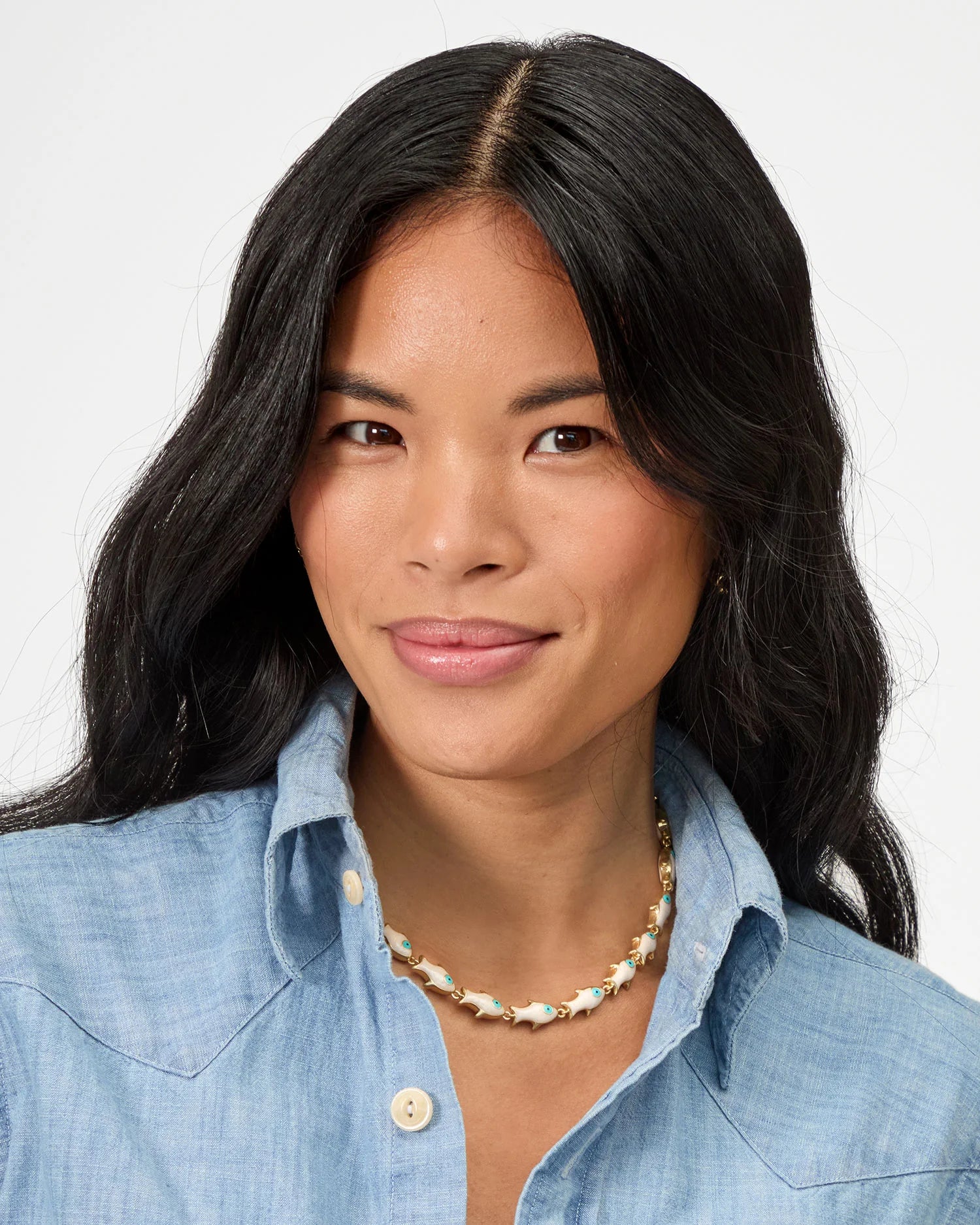Woman wearing a blue denim shirt and a necklace on a plain background