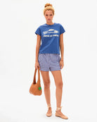 Woman wearing a blue t-shirt and striped shorts, holding a straw bag on a white background
