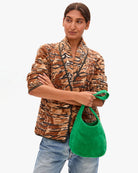 Woman wearing a patterned jacket holding a green bag on a white background