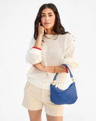 Woman wearing a white sweater and beige shorts, holding a blue handbag on a white background