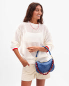 Woman holding a blue handbag with red accents against a white background