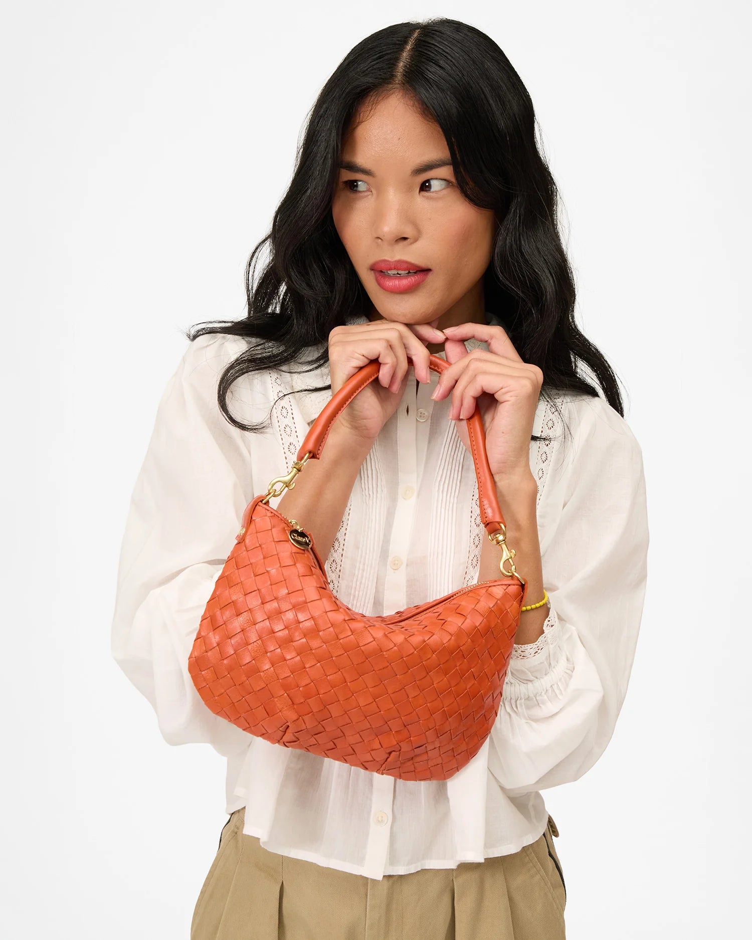 Woman holding an orange woven handbag against a white background