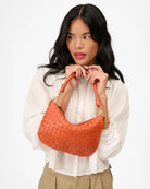 Woman holding an orange woven handbag against a white background