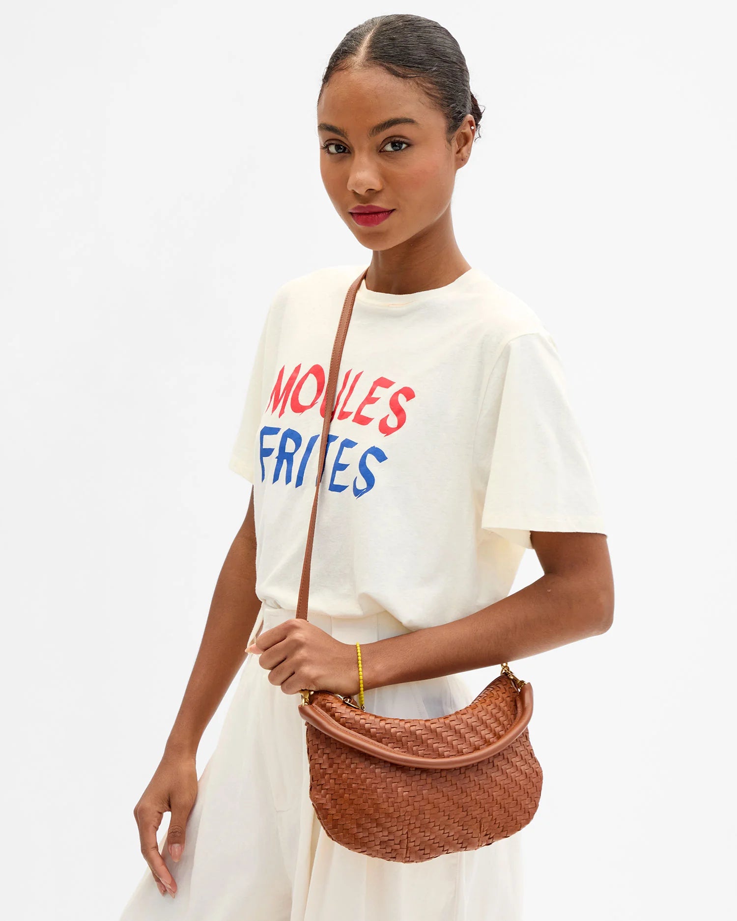 Woman wearing a white t-shirt with colorful text and holding a woven handbag against a white background
