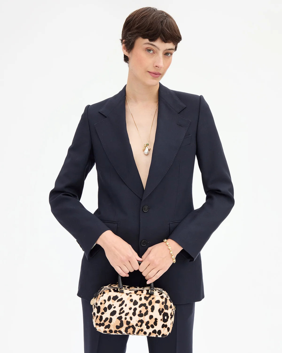 A model wearing a dark navy blue tailored blazer and matching trousers, holding a leopard-print handbag against a plain white studio background.