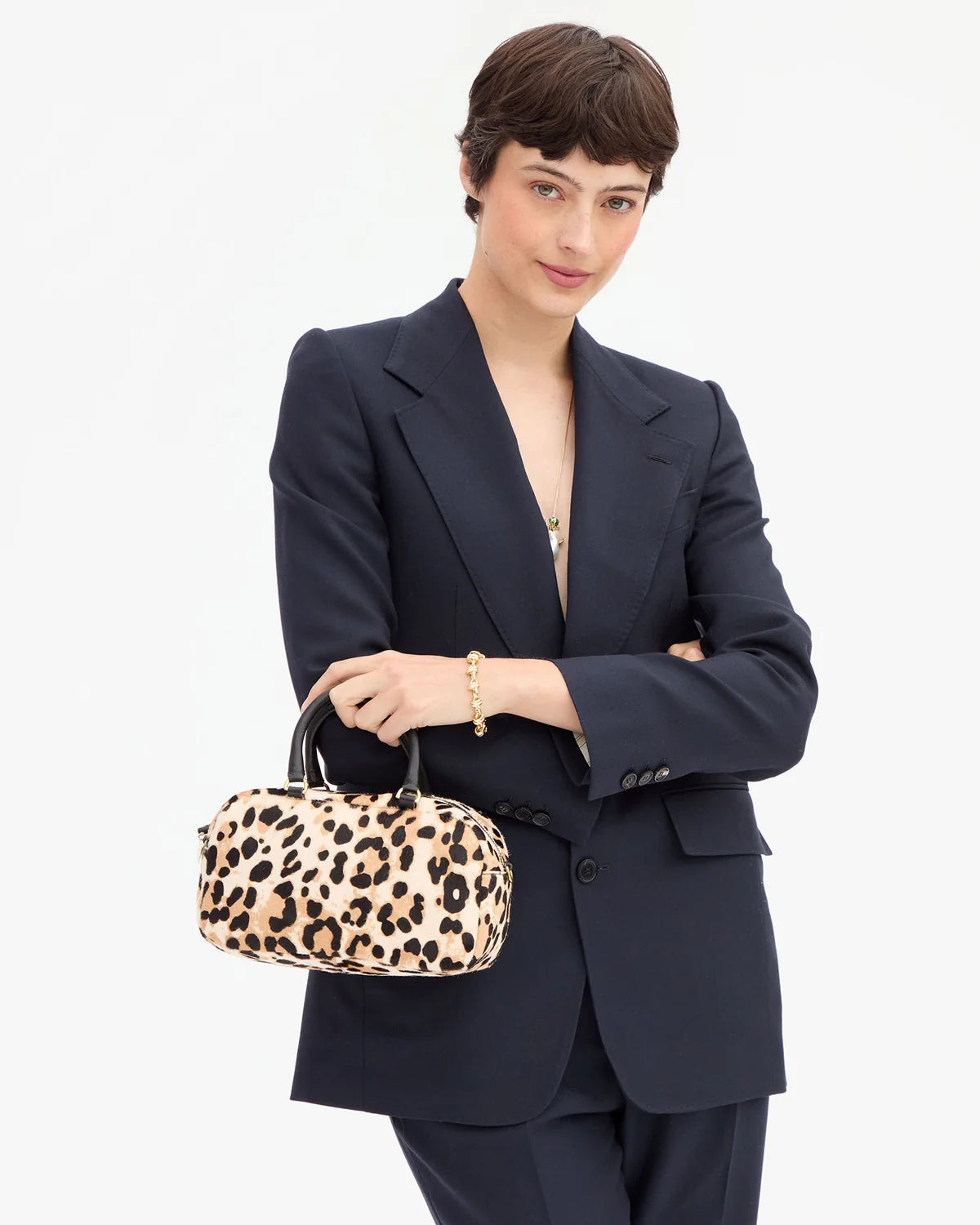 A model wearing a navy blue tailored suit holds a leopard-print handbag with black handles against a clean white background.