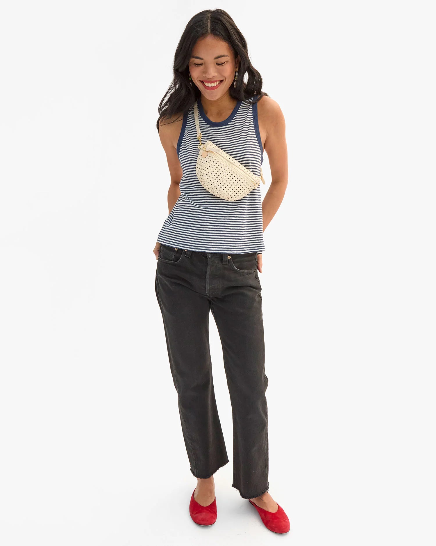 Woman wearing a striped tank top and black jeans, standing against a white background