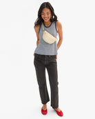 Woman wearing a striped tank top and black jeans, standing against a white background