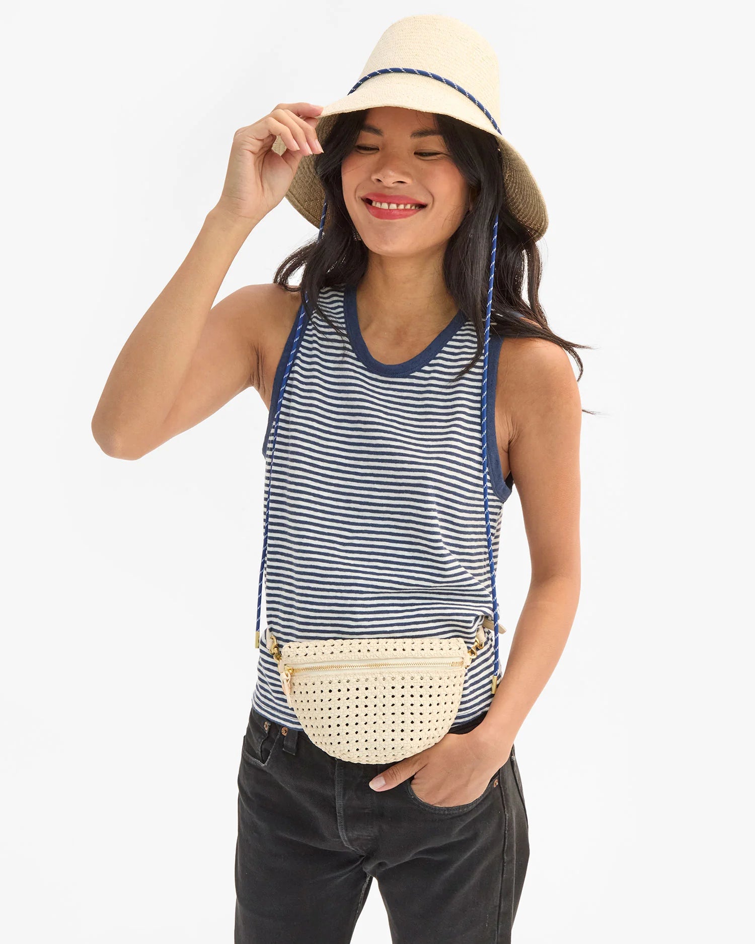 Woman wearing a striped tank top, black pants, and a straw hat with a beige woven belt bag.