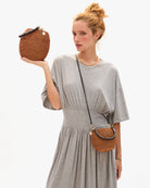 Woman holding a woven handbag and wearing a matching crossbody bag against a white background