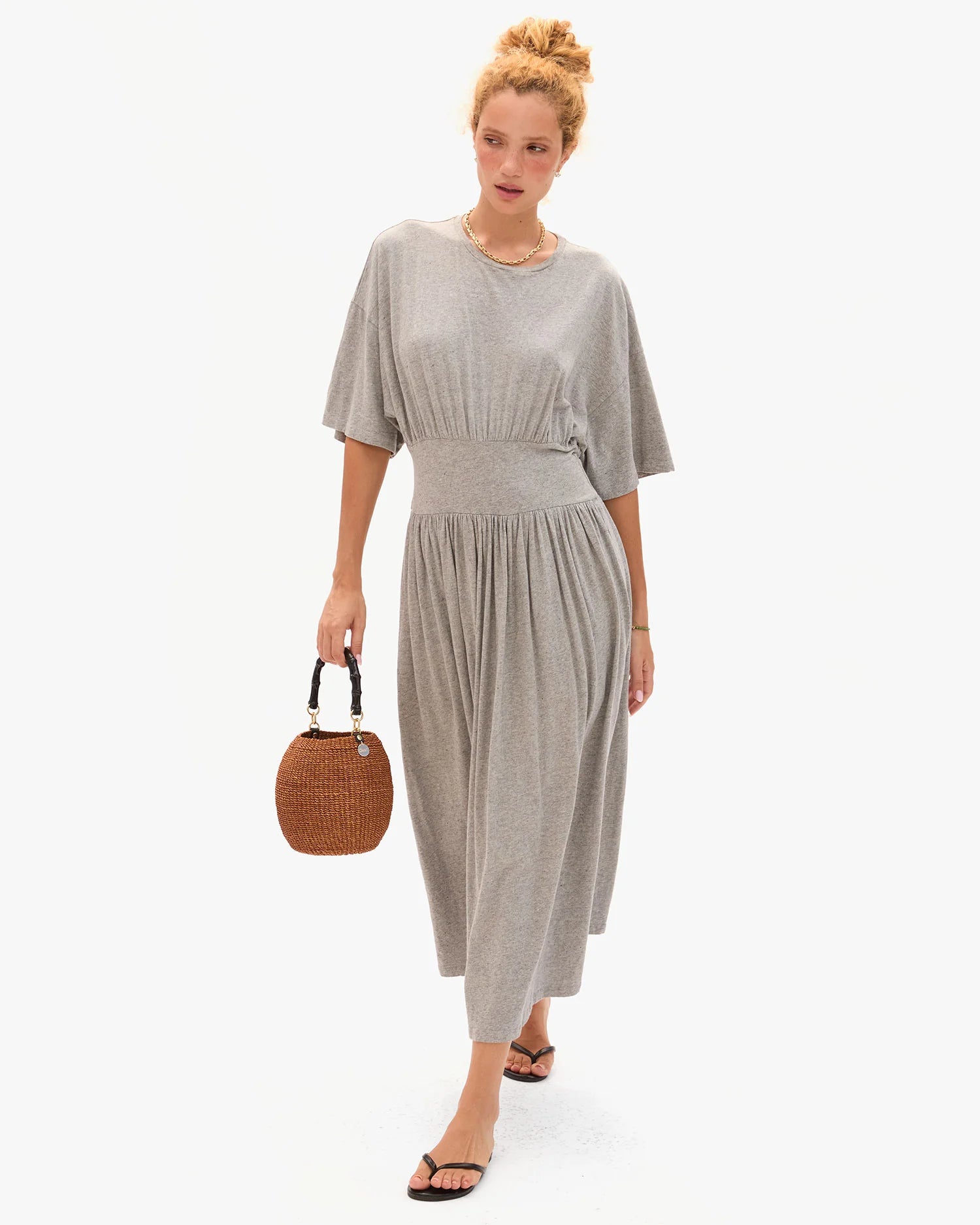 Woman wearing a gray dress holding a woven handbag on a white background