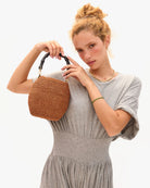 Woman holding a woven handbag against a plain background