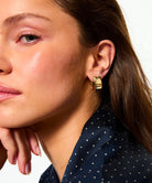 Close-up of a woman wearing gold hoop earrings with a neutral background