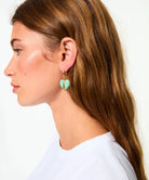 Close-up of a person wearing turquoise heart-shaped earrings with a plain background
