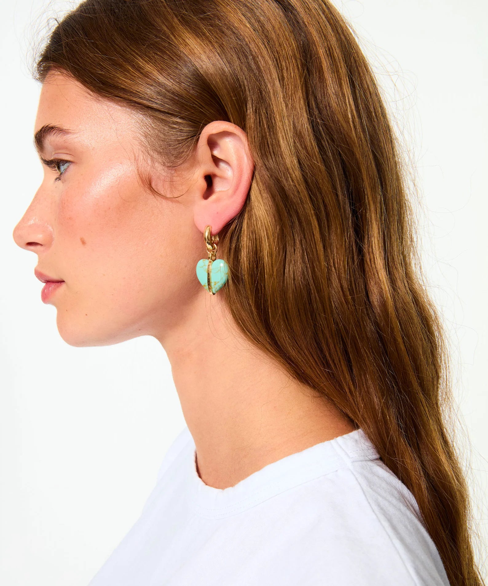 Close-up of a person wearing turquoise heart-shaped earrings with a plain background