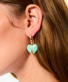 Close-up of a person wearing a gold heart-shaped earring with a turquoise stone.