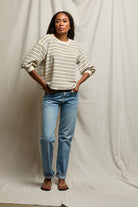 Person wearing a striped sweater and blue jeans against a plain background