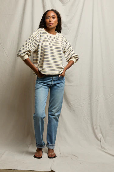 Person wearing a striped sweater and blue jeans against a plain background