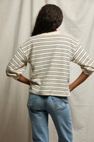Person wearing a striped shirt and jeans standing against a plain background