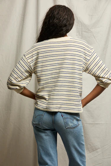 Person wearing a striped shirt and jeans standing against a plain background